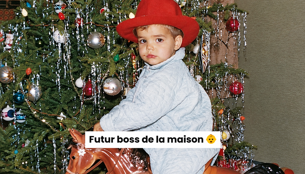 Enfant avec un chapeau rouge sur un cheval à bascule devant un sapin de Noël